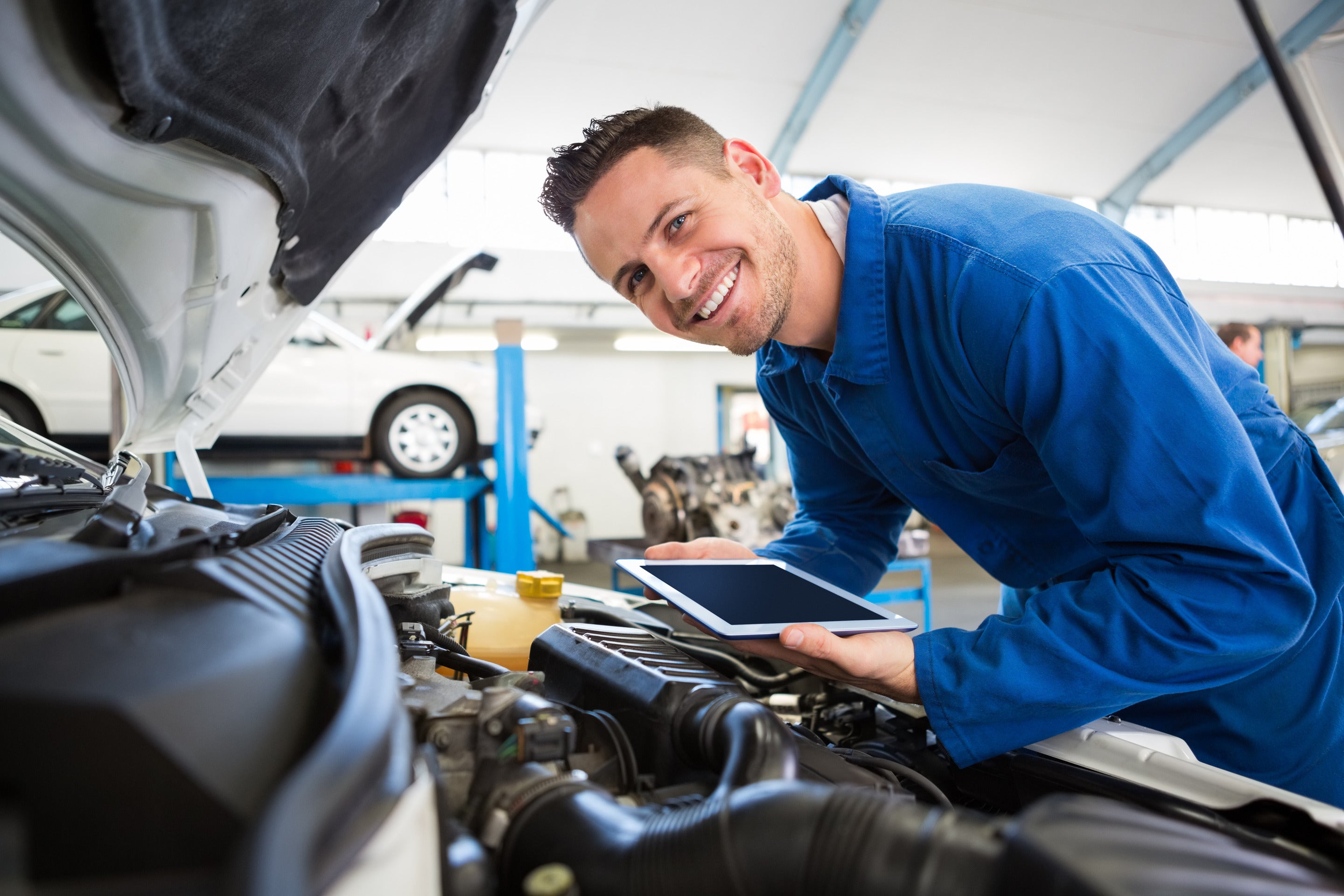 Technician wearing blue shirt holding an ipad inspecting a vehicle